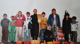 A group of children in costumes stand in front of carved pumpkins at Halloween time.