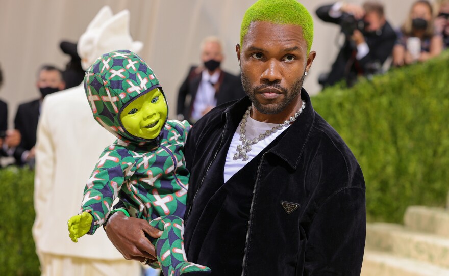 Frank Ocean, wearing a Prada suit jacket, carries a ... green robot-puppet-doll? A <a href="https://shrek.fandom.com/wiki/Ogre_Triplets#:~:text=Fergus%2C%20Farkle%20and%20Felicia%20are,Forever%20After%2C%20and%20Scared%20Shrekless.">baby Shrek</a>? We're just as confused as y'all are.