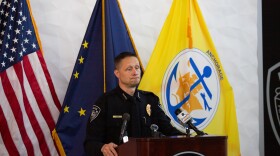 A police man speaking behind a podium with flags in the back