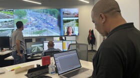 Johnson on a laptop in front of a bunch of screens looking at different intersections throughout the county, with some other people staring at the screens in front of him. 