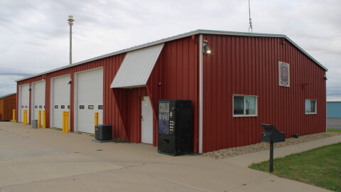A picture of the outside of a fire department in a rural area. The building is red with white doors.