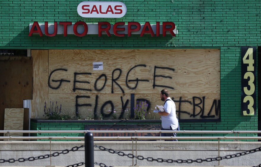 A mail carrier walks by a boarded-up business in the ethnically diverse Frogtown neighborhood of St. Paul, Minn., during continued demonstrations against the killing of George Floyd.