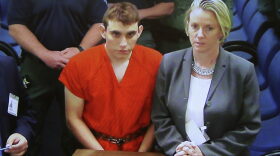 A video monitor shows school shooting suspect Nikolas Cruz, left, making an appearance before Judge Kim Theresa Mollica in Broward County Court, Thursday, Feb. 15, 2018, in Fort Lauderdale, Fla. Cruz is accused of opening fire Wednesday at the school killing more than a dozen people and injuring several. (Susan Stocker/South Florida Sun-Sentinel via AP, Pool)