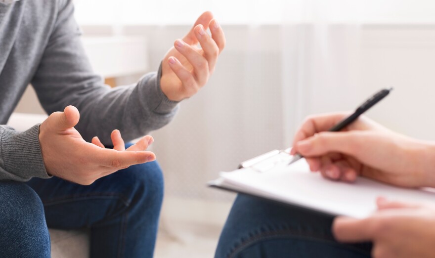 Psychotherapist writing notes, assessing patient's health and giving diagnosis to man sitting on couch during counseling session , panorama, free space.