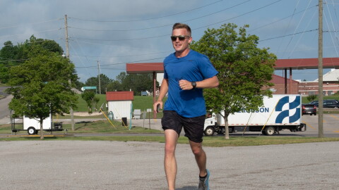 U.S. Air Force Capt. Alex Klinner wears a blue shirt and black shorts as he jogs along a road.