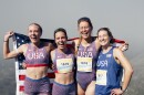 Four women in USA-themed running outfits and sneakers pose at the top of a mountain, with an American flag behind them.