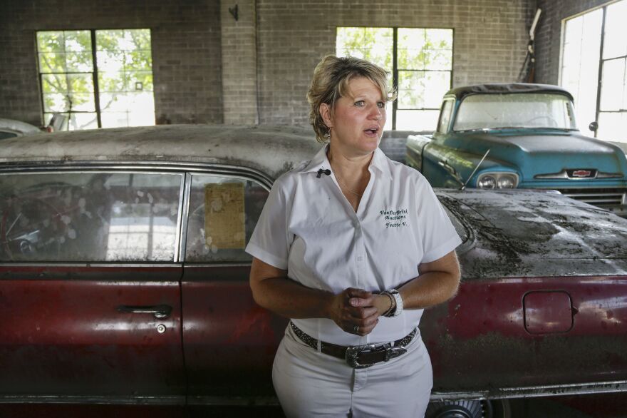 Auctioneer Yvette VanDerBrink in front of a 1963 Chevrolet Impala and a 1958 Cameo pickup truck at the Lambrecht Chevrolet car dealership.