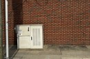 A beige metal box about the size of a deep freezer sits in front of a red brick wall.