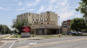 A bright red electric sign identifying Carle Health Pekin Hospital stands at an intersection with the large medical building in the background. 