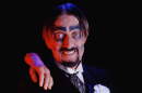 Man dressed in a costume with black suit and a severed hand on his shoulder 