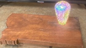 A wooden cutout in the shape of Montana with a colored full-size light bulb.
