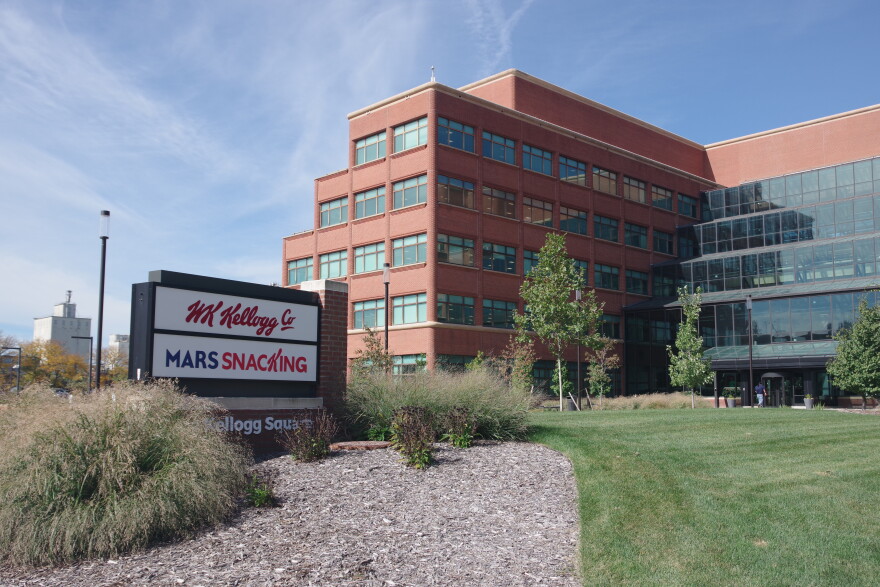 A sign saying "W.K. Kellogg Co" and "Mars Snacking" is displayed in a garden bed in front of a multi-story brick building.