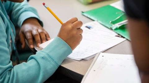 A student writes with a pencil at a table.