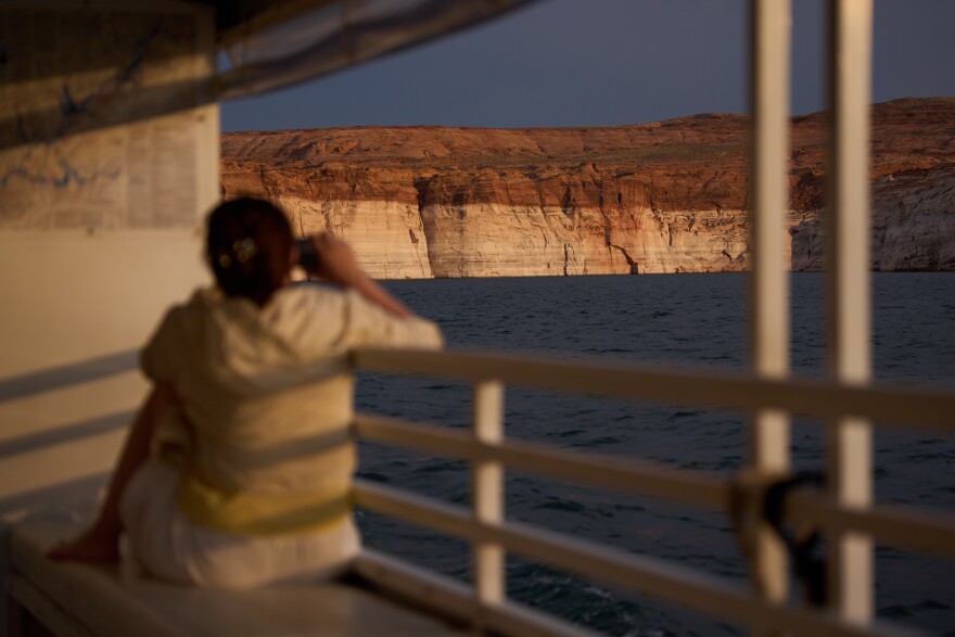 A person takes a picture during a tour on Lake Powell at the Glen Canyon National Recreation Area, Wednesday, July 15, 2026, near Page, Ariz. A bathtub ring of light minerals on the canyon wall shows the high water mark of the reservoir.