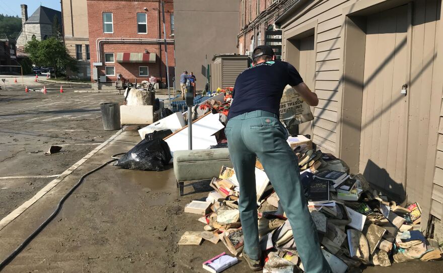 A person leans away from the camera and dumps a box onto a pile of books outdoors