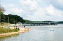 A wide shot of a beach and lake. People are lounging on the sand and in the water. 