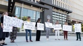 A group of people hold signs protesting a law making it a crime for transgender people to use the restroom that aligns with their gender identity.