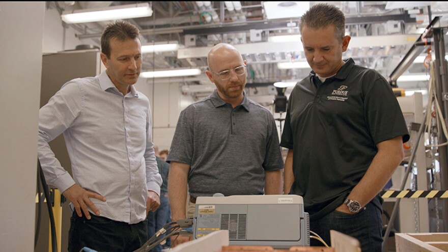 Aaron Brovont (middle) and other engineers seen in a lab surveying technology that can charge electric vehicles.
