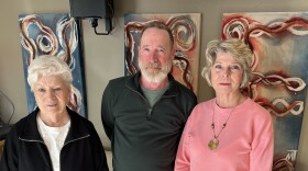 Three people wearing a black, green and pink sweatshirt standing in front of blue and red paintings