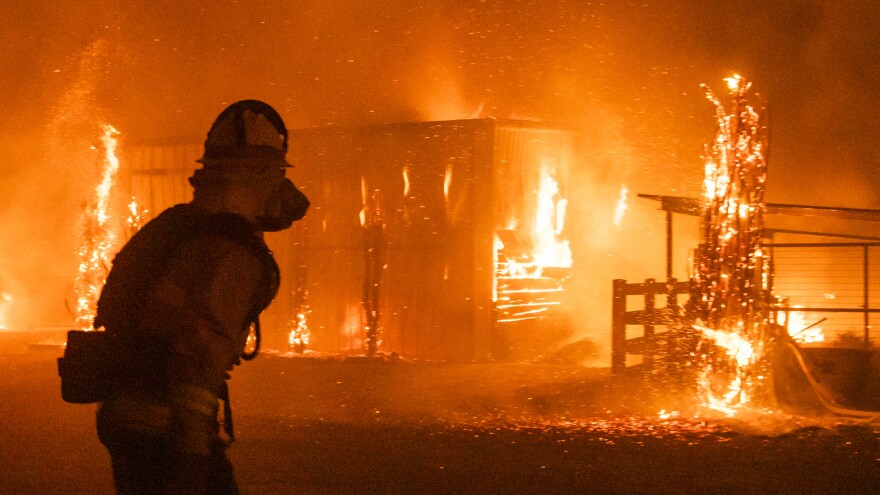 Firefighters look on as a blaze tears through structures on a farm Sunday in Windsor, Calif., where the Kincade Fire has driven residents from their homes.