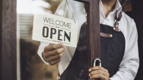 Store owner turning open sign broad through the door glass and ready to service.