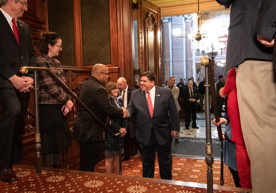 Gov. J.B. Pritzker shakes hands with lawmakers as he enters the Illinois House chamber for his annual budget speech