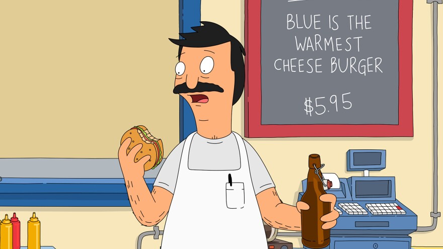 Bob Belcher, titular hero of <em>Bob's Burgers,</em> bites into one of his creations. Each episode features daily burger specials with chuckle-inducing names. The burgers were born in the show writers' imagination and brought to life in Cole Bowden's kitchen.