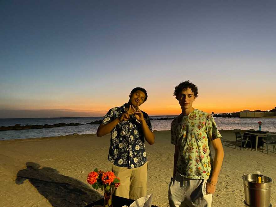 Two boys stand on a beach at sunset.