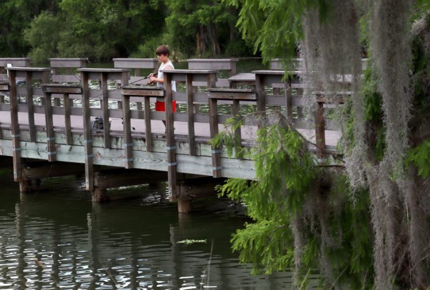 A child holds a fishing pole off the side of a wooden pier.