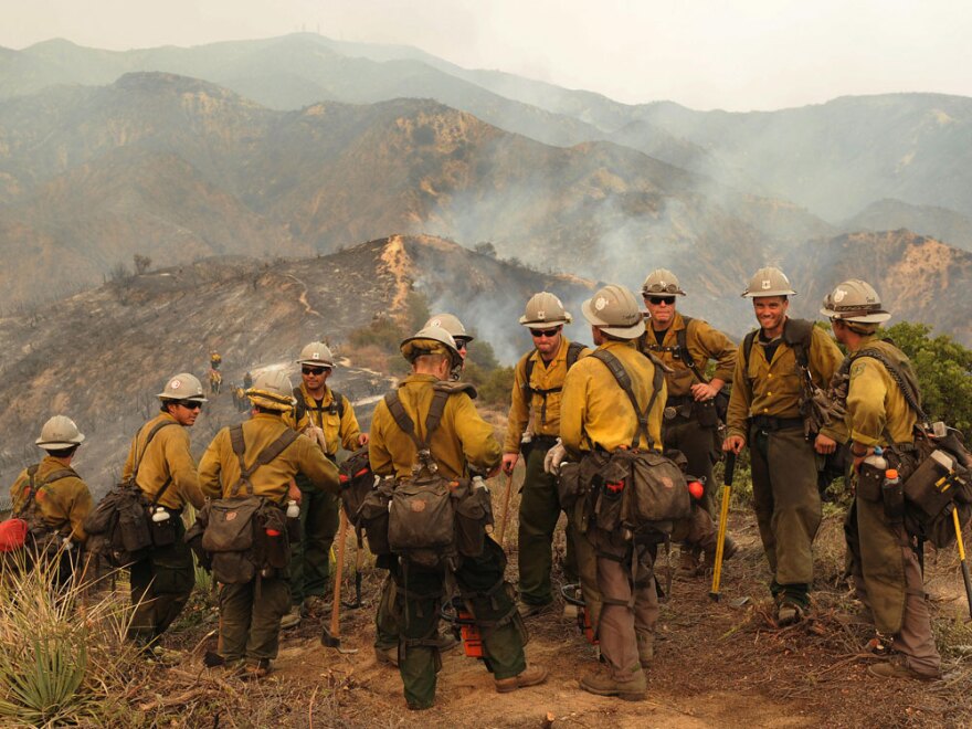 Firefighters take a break Monday near the suburb of Glendale on the outskirts of Los Angeles. Since erupting Aug. 26, the Station Fire has destroyed more than five dozen homes and forced some 12,000 residents to flee.