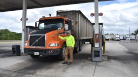 A trucker in a highlighter-yellow shirt smiles next to his truck. 