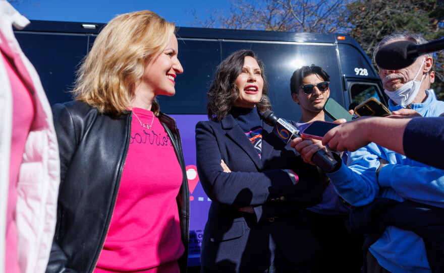 Democratic gubernatorial nominee Jocelyn Benson, left, and Gov. Gretchen Whitmer, right, speak with reporters in East Lansing, Mich., during the first stop on Benson's statewide "Driving Down Costs" bus tour on Oct. 22, 2026.