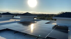 Solar panels on a residential rooftop with the sun round and blazing above it. 