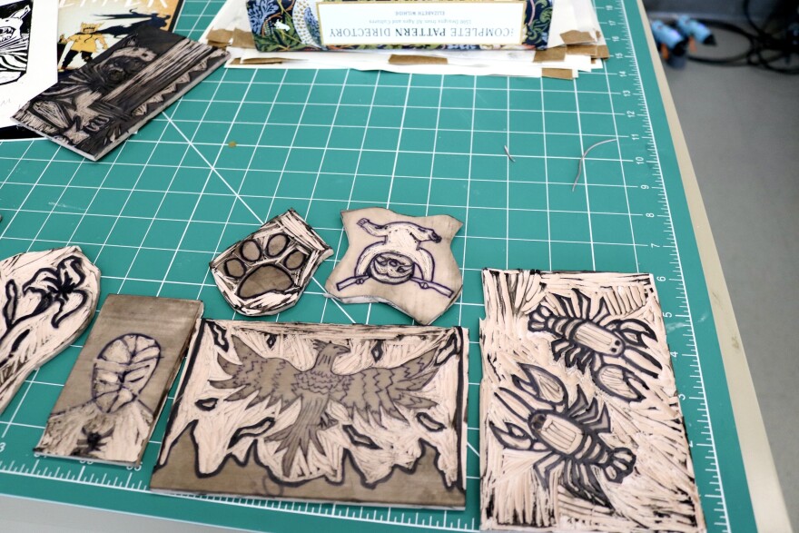 A series of rubber stamps lay on a classroom table, all with a different design: a pair of lobsters,  a bird with its wing’s spread, a sloth, a dog’s pawprint, Spiderman, and a flower.