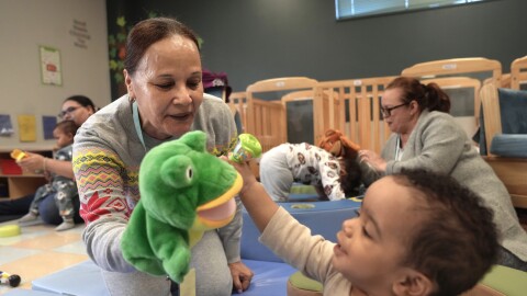 A woman uses a frog puppet for entertainment while supervising 10-month-old, front right, in an early childcare program at Federal Hill House.