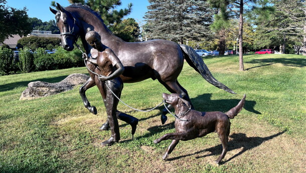Statue of a girl walking a horse alongside a running dog.