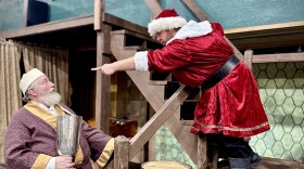 A man in a Santa costume pointing and yelling at a man with a white beard wearing a robe and holding a large chalice.