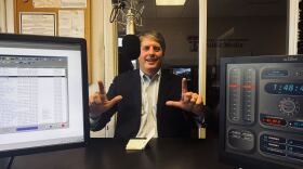 A photo of Tom Sell in the KTTZ studio. He is smiling and doing the Texas Tech 'guns up' hand sign.