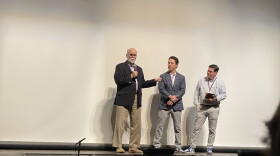 Three men stand on a stage.