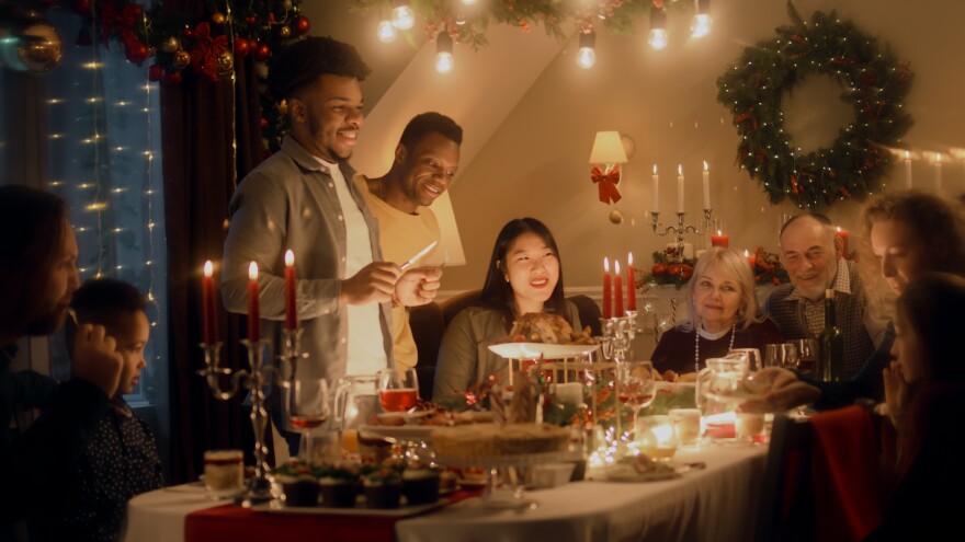 African American man cuts turkey with knife. Multi cultural family celebrating Christmas or New Year. Served holiday table with dishes and candles. Warm atmosphere of family Christmas dinner at home.