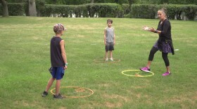 A female PE teacher with two young male students. They are standing next to three holahoops in a grass yard. 