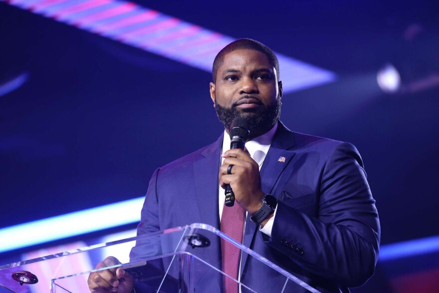 African American man in blue suit holds microphone at podium 