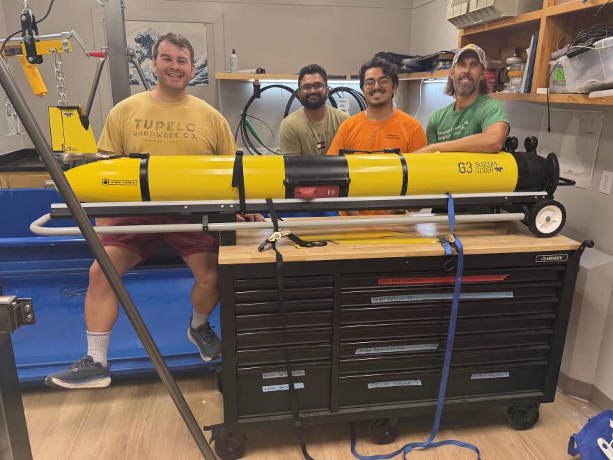 Four men stand in front of a glider in a lab.
