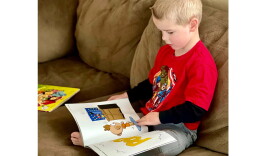 Bjorn Alder, a Lewiston recipient of the Dolly Parton Imagination library, reads cross-legged on a couch.