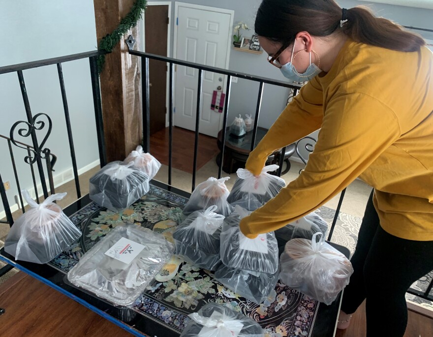 A woman in a yellow shirt organizes food in separate plastic bags. She is standing in a house and the food is on a table.