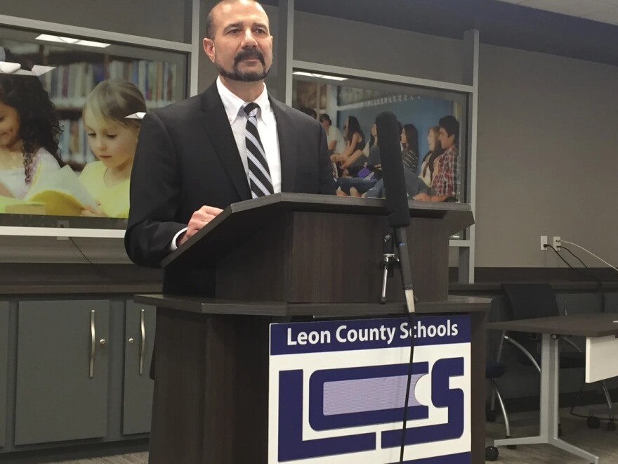 A man wearing a suit and tie, standing at a podium behind a sign that says 'Leon County Schools'