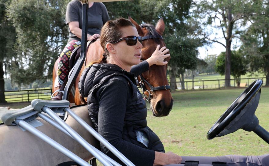 Ashley Johnson coaches her students from a golf cart while wearing a knee brace on Friday, Nov. 3, 2023. She carts a pair of crutches with her following a knee injury she suffered while training young horses two days prior at her barn in Ocala, Fla. “I’ve had veterinarians X-ray me before, instead of going to the hospital,” Johnson said. “Horse people are crazy…I was back on a horse as soon as I could walk which was about a week in.”