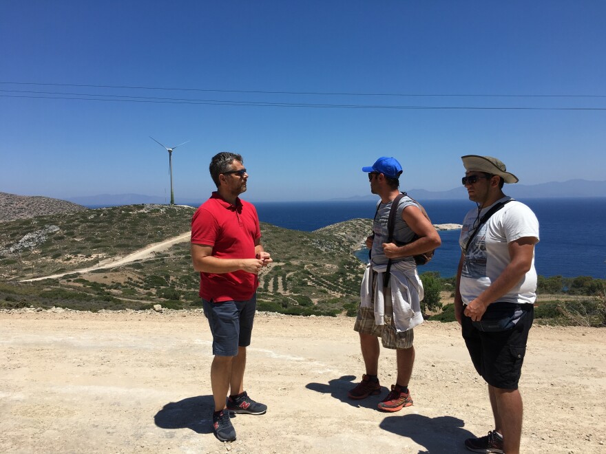 Stathis Kontos, who works for the Tilos municipality, talks to two tourists about the clean energy project after they spot the wind turbine in the distance.