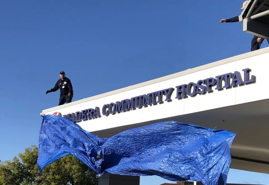 Workers atop the roof above the emergency room entrance at Madera Community Hospital dropped tarps that had covered the hospital’s name since it closed in January 2023. The unveiling was part of opening ceremonies for the hospital on Tuesday, March 18, 2025.