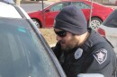 A police officer leans onto the driver's side of a car, speaking with that driver. 